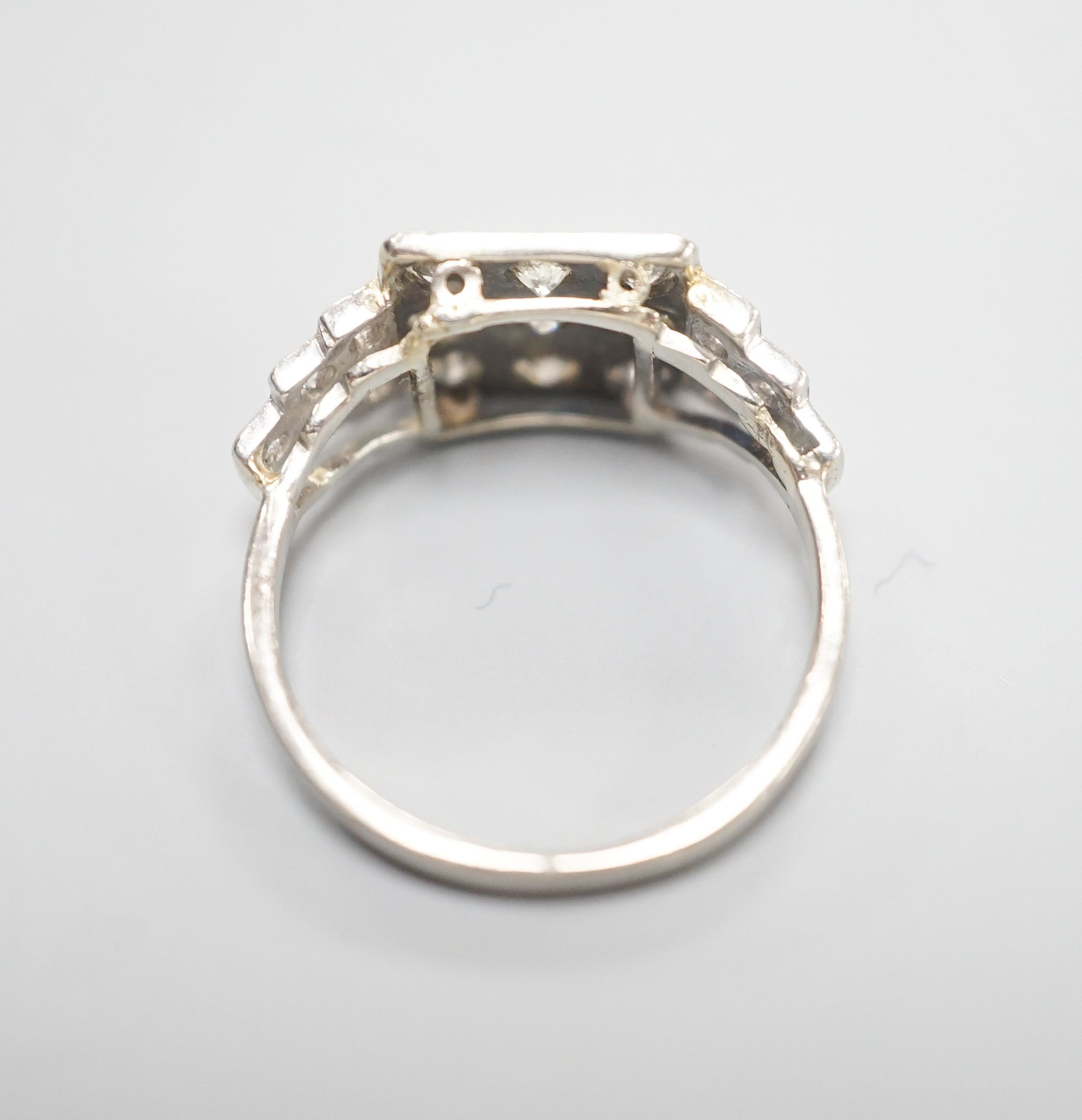 An Art Deco style white metal and nine stone diamond set tablet ring, with diamond set stepped shoulders, size K, gross weight 3.2 grams.